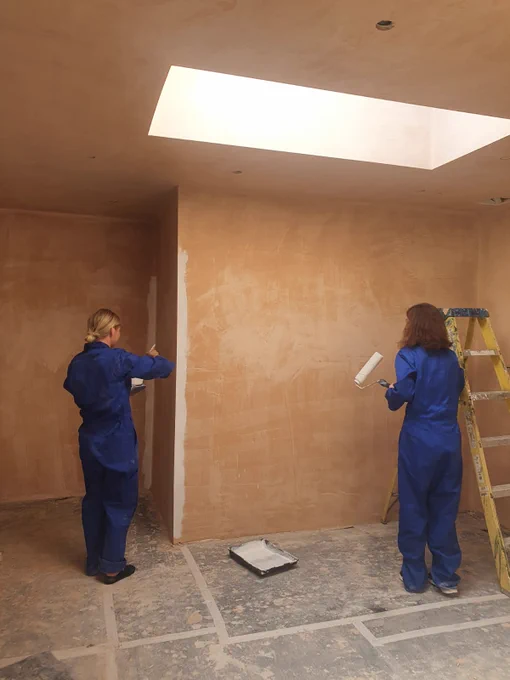 Two volunteers stand inside the wash block holding paint rollers
