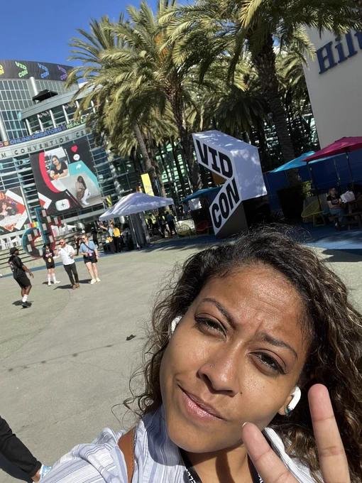 Brittni flashing the peace sign in front of a vidcon display