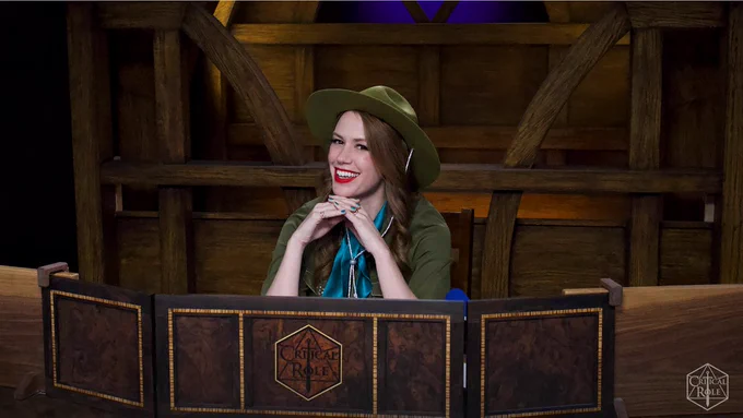 Marisha Ray sitting behind the Critical Role game master screen in a park ranger outfit 