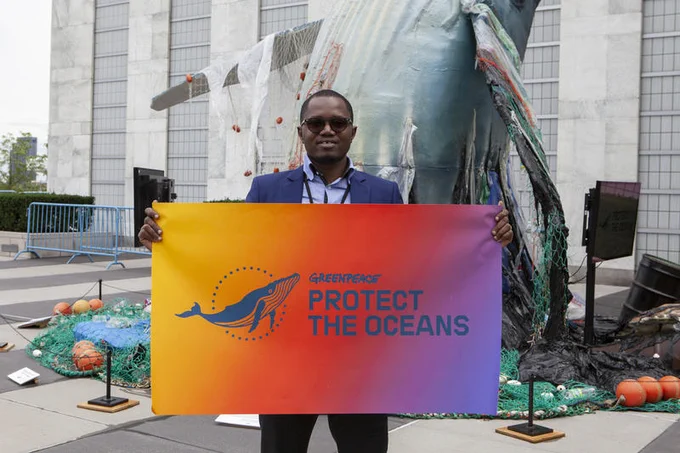 Dr Aliou Ba, (Campaigner, Greenpeace Africa) holding a 'Protect The Oceans' banner in front of an Ocean-inspired artwork created by Greenpeace 