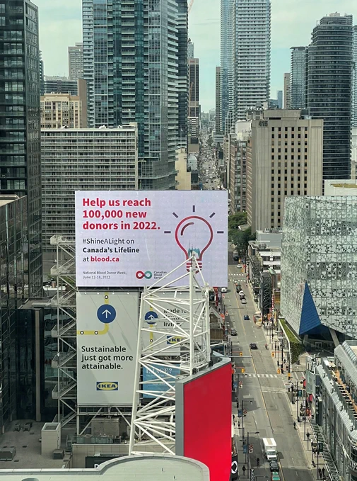 Billboard in downtown Toronto says Help us reach 100,00 new donors in 2022 - Canadian Blood Services (image of a light
bulb)