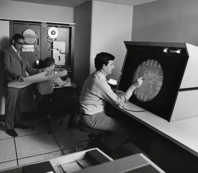CBI Image of the Day. Black and white square photo. Design and testing of circuitry at Microcircuits Laboratory. Frans Ucko on left, Manager of Microphoto & Computer Graphics. Circa 1960s. Many seated at oscilloscope circular large screen similar to those used by the Air Force and at RAND using a light pen to aid design of circuits on screen.  In the foreground there is the edge of drawer that holds punch cards. One man sits in the background in front of a paper tape reader, Manager Frans Ucko stands looking at a large sheet of designs, likely of circuits.