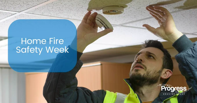 Image shows a man in a hi-vis vest looking at a smoke alarm. Home Fire Safety Week in a blue box..