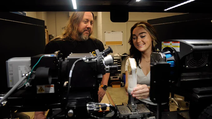 Two people looking at a rock sample in a lab machine.