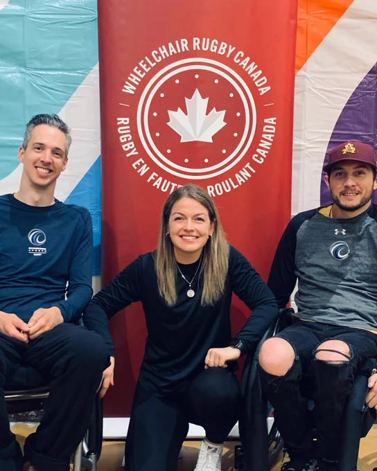 Wheelchair Rugby coaches Byron Green, Kendra Todd and Trevor Hirschfield smile in front of a red Wheelchair Rugby Canada banner. 