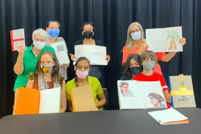a group of children and adults wearing masks shows off the books they made in a bookmaking Big Read workshop