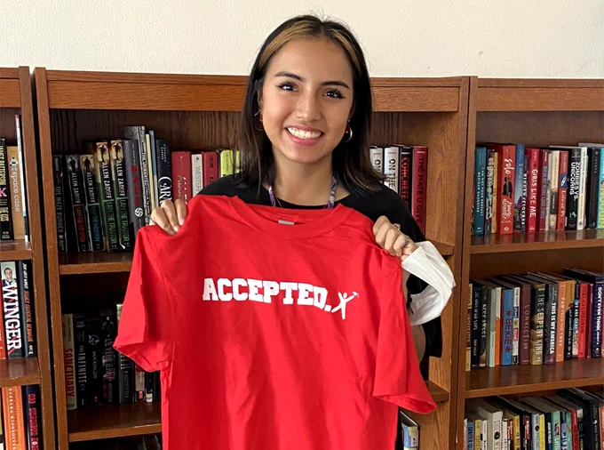 Female student holds up a t-shirt that says "Accepted" on it to signify her college acceptance. 