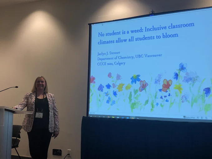 Woman standing by PowerPoint presentation- titled No Student is a weed: Inclusive classroom climates allow all students to bloom