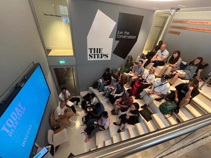 A picture of a group sitting on the steps in front of speakers for an event.