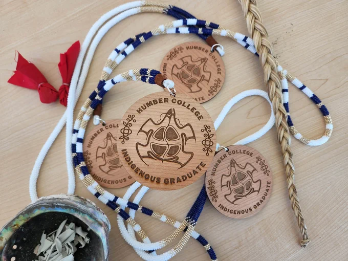 A collection of medallions that read Humber College Indigenous Graduate sitting on a table.