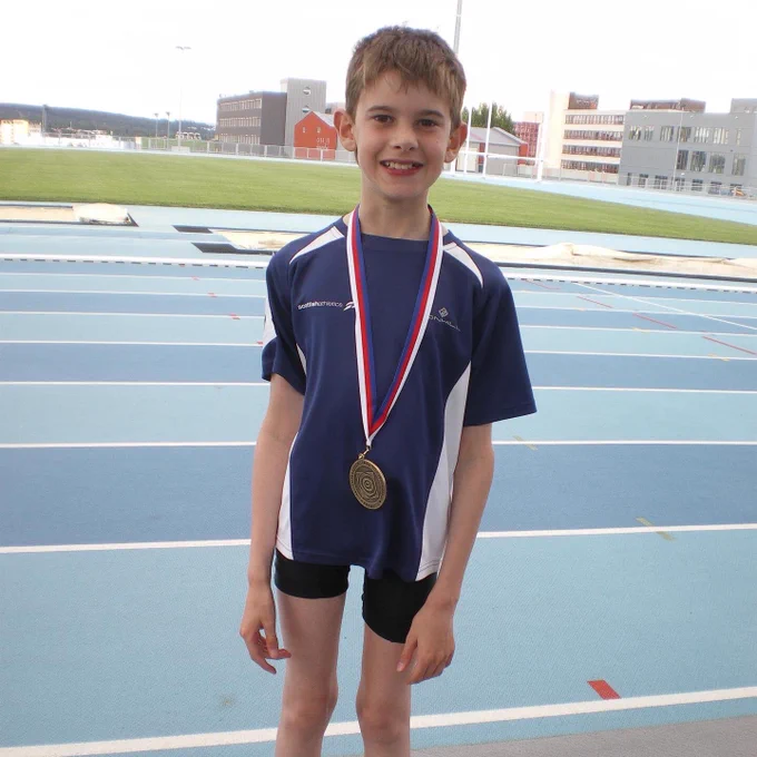 A young Gavin standing proudly with a gold medal round his neck. Blue track in the background