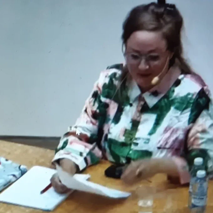 Amazing Josefin in a fabulous blouse and fancy headset microphone sits at a table in zoom preparing for her dissertation defence. 