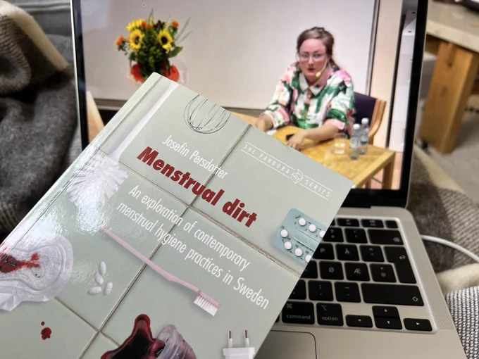 The book and PhD thesis “Menstrual Dirt” being held in front of a computer screening the PhD defense of author Josefin Persdotter.