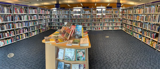 Three sides of a square made by bookshelves at the Millennium Library, with an island display unit in the centre, featuring books about sport.