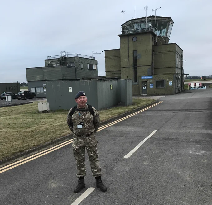 Image shows a man in front of an air traffic control tower.