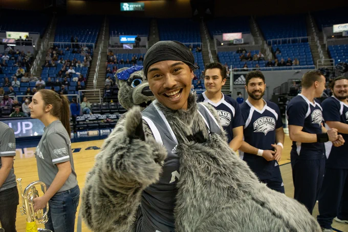 Nevada Wolf Pack Mascot, Alphie, revealed as University of Nevada, Reno student Nolan Caberto, pointing to the camera with the cheer team behind him in Lawlor Events Center. 