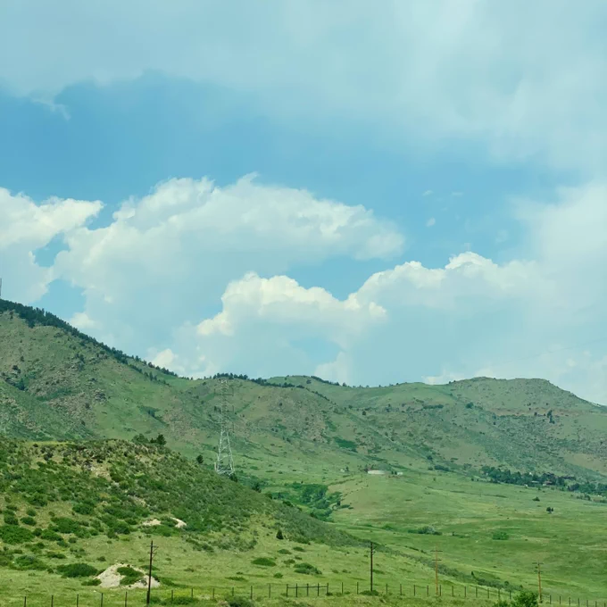 A picture of the green rolling mountains of Colorodo with large fluffy clouds in the sky. 