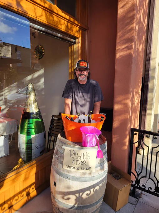 Cider brewer Dave Carr standing behind a keg barrel with a bucket of iced bottles of his own @ragingcider ready to serve.