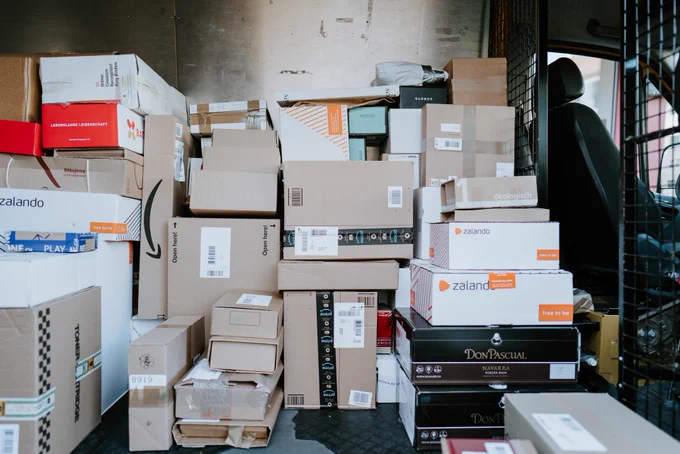 The back of a delivery truck stuffed with cardboard packages, piled on top of each other. Photo by Claudio Schwarz on Unsplash.