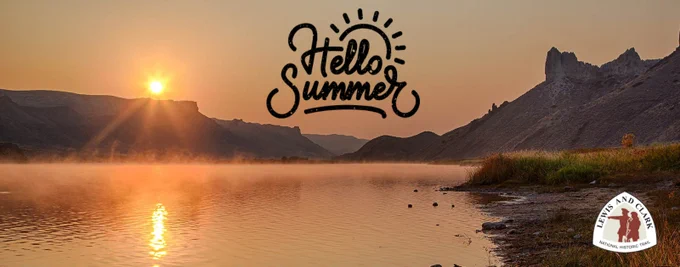 The orange hues of the setting sun silhouetting the edges of the White Cliffs of the Upper Missouri River Breaks National Monument.  A mist rises off the river’s surface.  In the center of the sky is a graphic, “Hello Summer!”  The Lewis and Clark Trail logo is in the lower right-hand corner. 