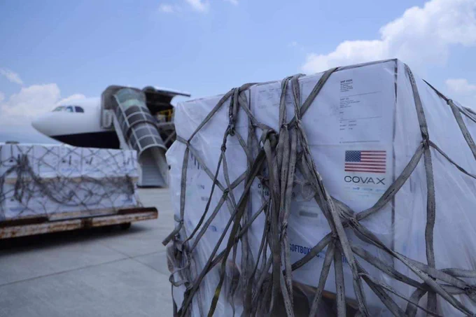 Boxes of vaccines sit on the tarmac with an airplane in the background.
