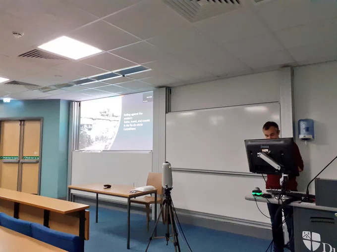 James at the front of the lecture theatre with a presentation on a projection showing a train in a black and white photograph 