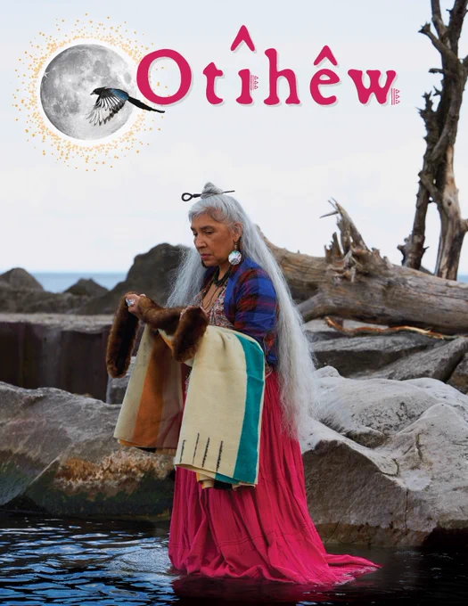 Monique Moijca wades into the water carrying hbc blanket and fur. Her long grey hair is tied half up into a top bun. She is wearing a vibrant pink skirt. The title Otîhêw is illustrated above her with an illustrated moon and magpie