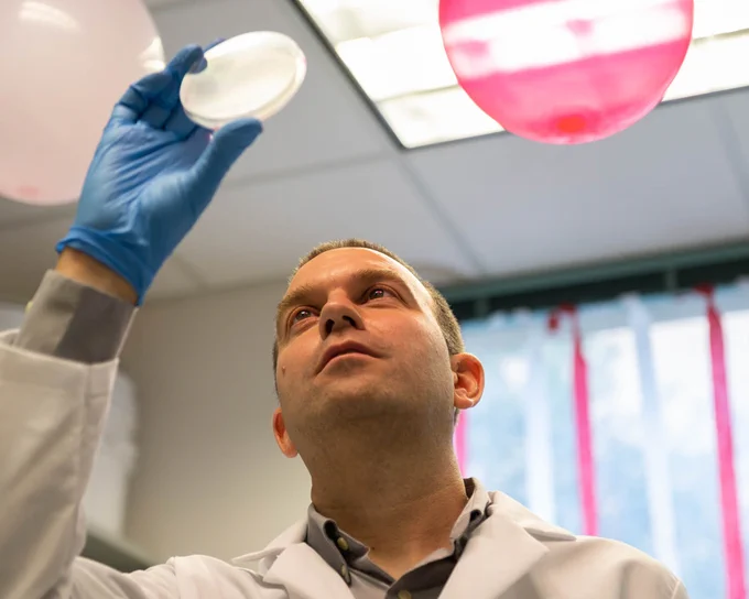 Jeffrey Barrick, a scientist at The University of Texas at Austin, holds a petri dish up to the light.
