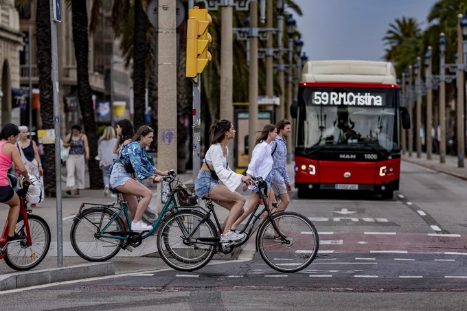Persones en bicicleta creuen un pas davant un autobús urbà aturat al semàfor.