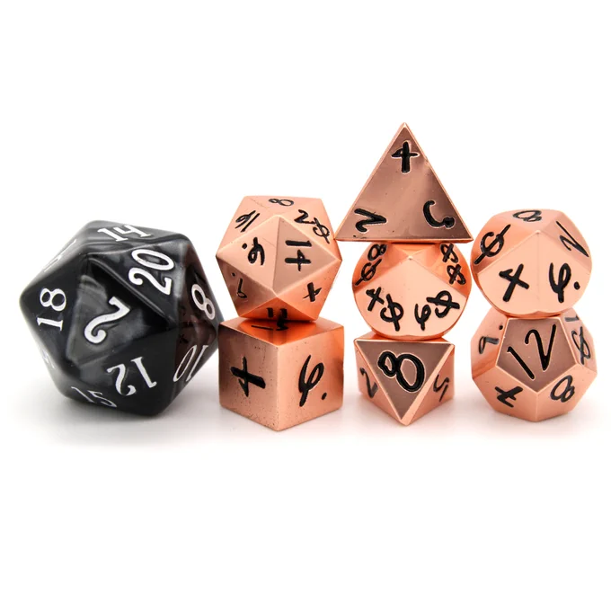 A 7 piece set of tiny 10mm rose gold metal TTRPG dice, the numbers in a black hand written font. Beside the tiny dice is a standard sized D20, for scale. It is nearly the same height as the tiny D20 stacked atop the tiny D6.