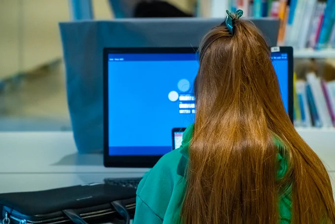 A teenage girl works at a computer screen; the photo is of the back of her head.