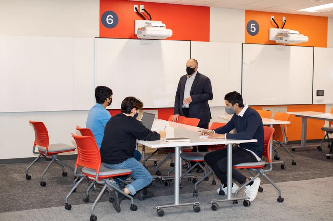 A professor in a classroom teaching three students at a desk.