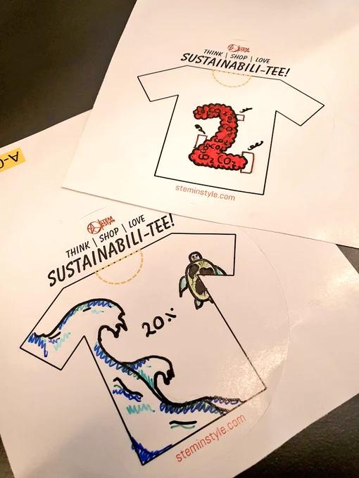 Two stickers printed with t-shirt shapes and student designs representing the polluting and waste impact of the fashion industry