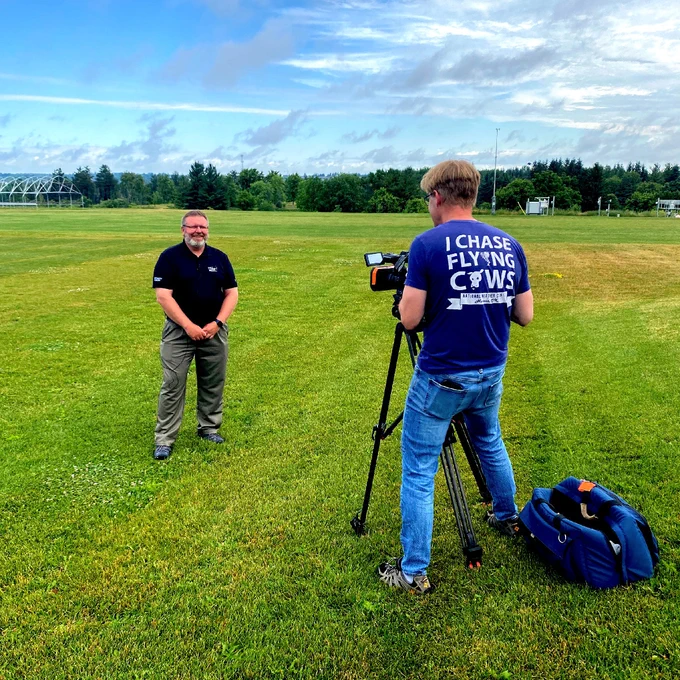 Eric Lyons stands in front of a camera, in front of a field of grass