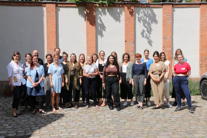 Gruppenbild von rund 25 fröhlich schauenden Personen in einem sonnigen Innenhof. 