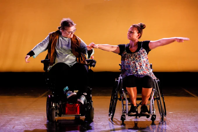 Two dancers in wheelchairs in a performance from Expressions 2019. The two dancers are looking at each other and holding hands. Photo by Brian Slater.