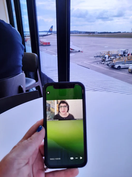 Hand holding phone in front a window with an airplane in background 