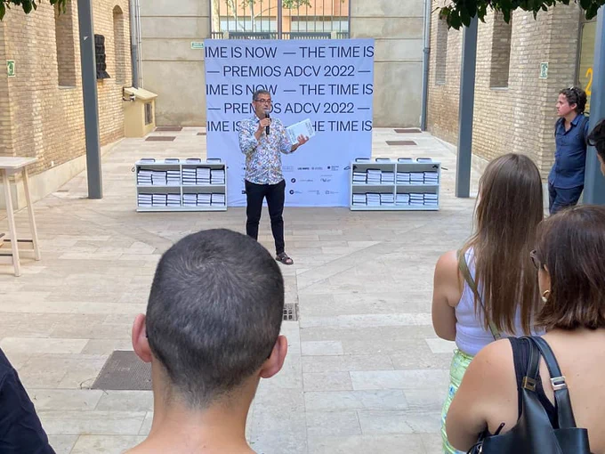 Fotografía del presidente de la ADCV, Ángel Martínez, presentando el libro Premios ADCV en el patio de Las Naves, con varios ejemplares