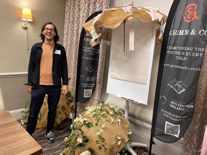Hugh, smiling in front of a flip chart and umbrellas decorated with leaves, flowers and bunting.