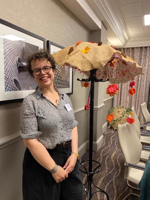 Jane, standing in front of a decorated umbrella covered in autumn leaves, propped open on a coat stand.