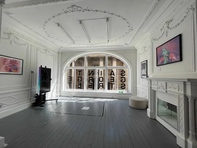 A room with a very large curved window with text decals on. The room is white and grand-looking, and has colourful artwork hung on the walls.
