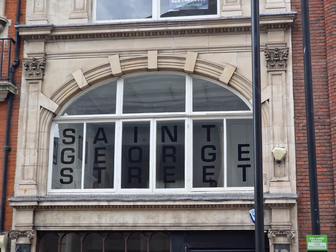 A large curved window with text decals on it, with the words "Saint George Street". The facade is grand and made of stone.