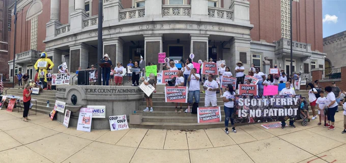 Photo of large crowd gathered on steps of York County Administration Building, many holding signs about Scott Perry