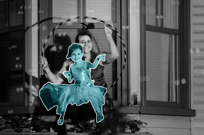 Ilana Bereskin and Ahava pictured sitting on a hoop. The little girl is highlighted in teal, with a white outline around her. She is wearing a dress with a tulle skirt, smiling, and looking towards the right side of the image. The older woman is holding the hoop, with the little girl in her lap. She is smiling, looking in the same direction as the camera. The full image, aside from the little girl is black and white.