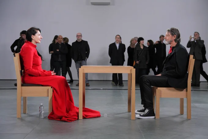 marina abramovic, an artist wearing a bright red dress, sits opposite her ex romantic and professional partner, ulay