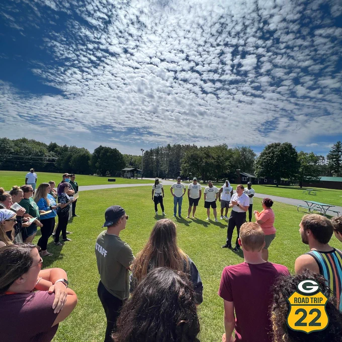 The Packers Road Trip stand in line as the the Wisconsin Lions Camp gathers to listen under a bright sky.