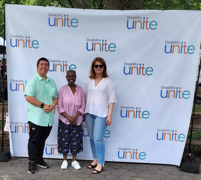 ICD's staff members, Stephen, Daria, and Katya smiling in front of a Disability Unite background.