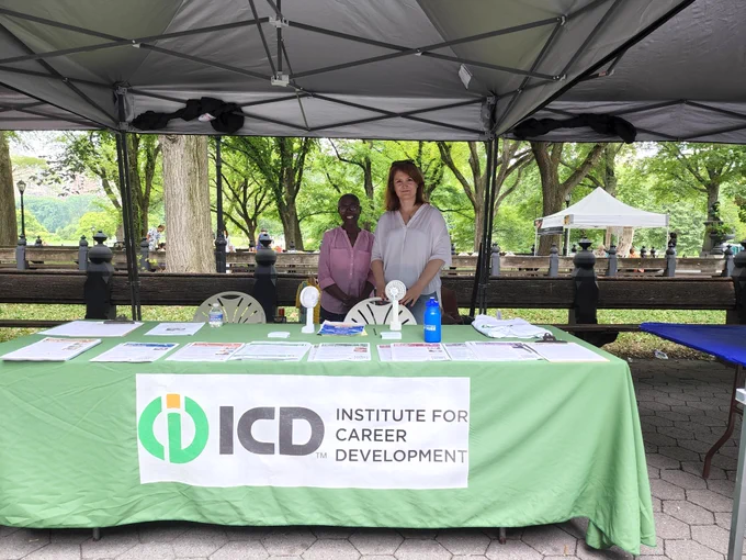 ICD staff members Daria and Katya standing behind an ICD table with a green table cloth and ICD logo with trees behind.