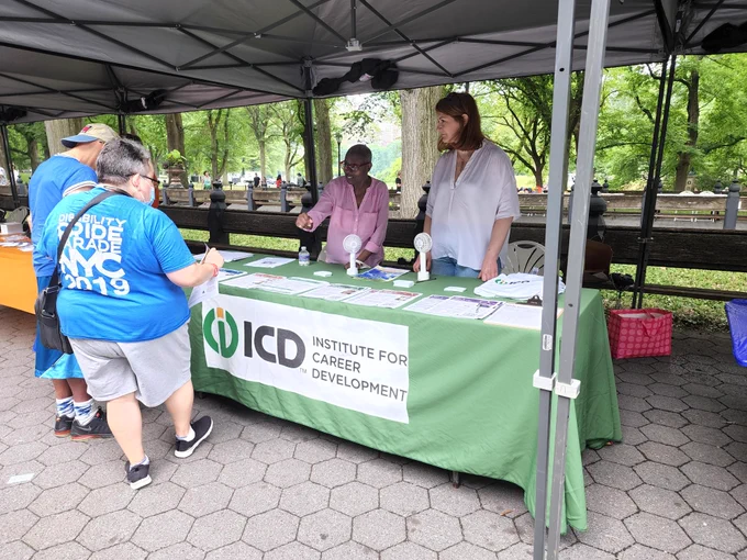 ICD staff members Daria and Katya standing behind an ICD table talking with two individuals. 