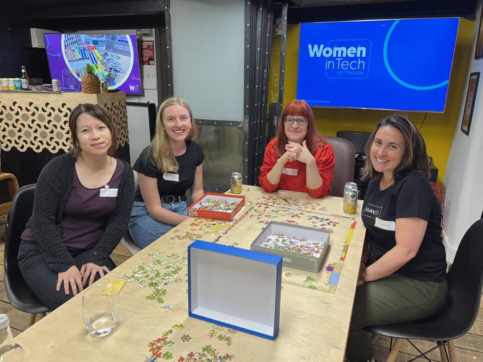 a group of women chatting and assembling a colourful abstract jigsaw